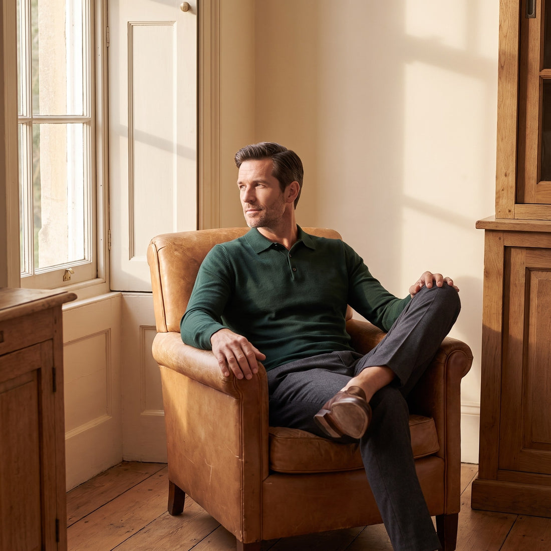 Man in a bottle-green knit polo seated in a leather armchair