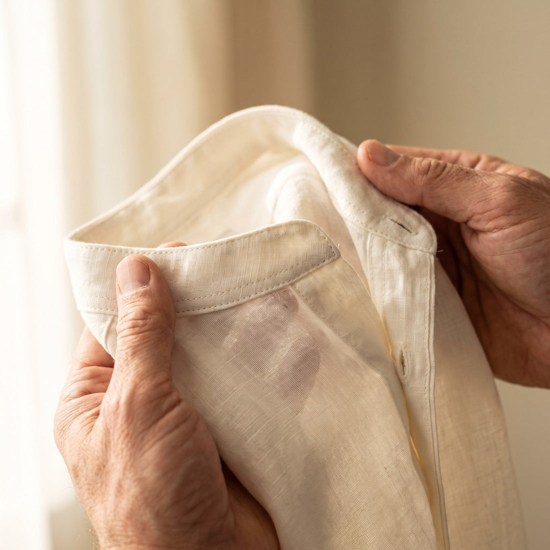 Hands checking the collar stitching of an ivory linen shirt