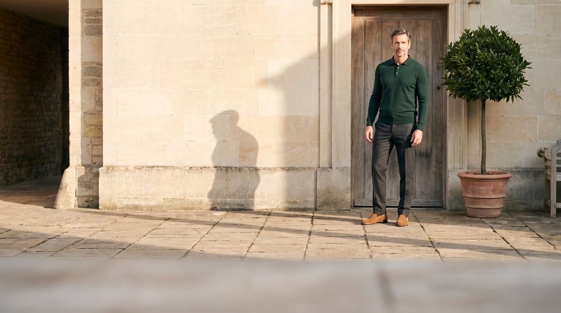 Man in a bottle-green knit polo in a sunlit stone courtyard